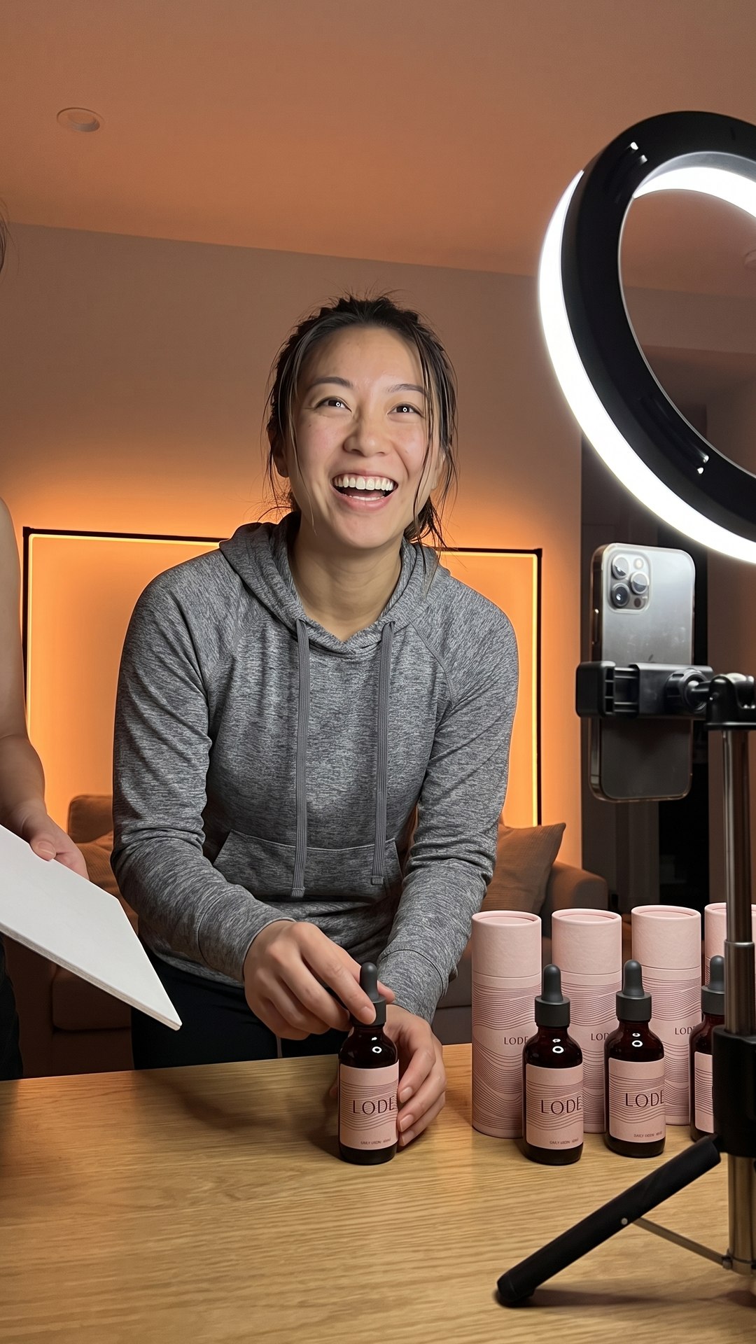 An athlete laughs between takes while filming content for her iron supplement, ring light and phone tripod in front of her.
